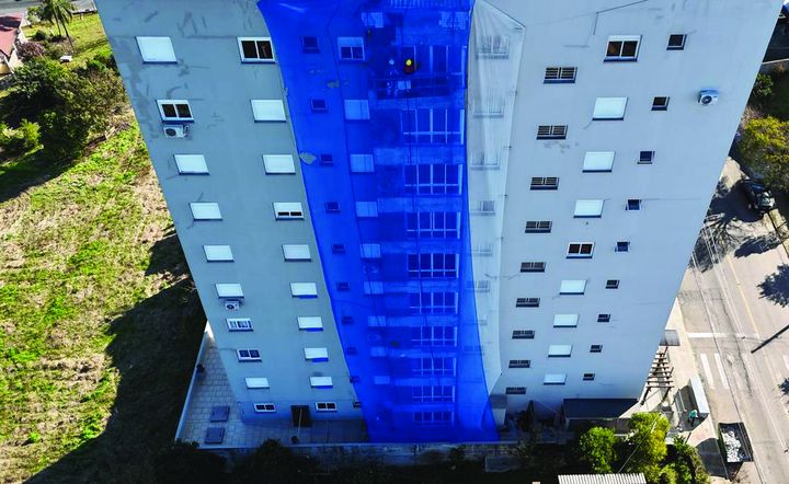 Vista aérea de edifício com tela de proteção azul na fachada durante obra
